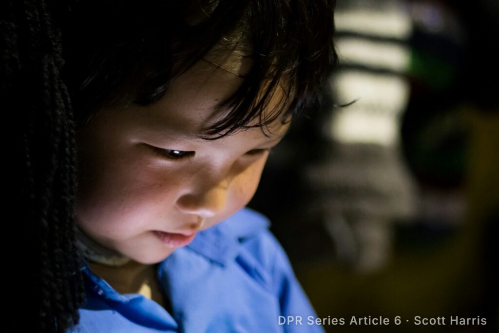 Young child’s face lit by the glow of a screen in a dark room