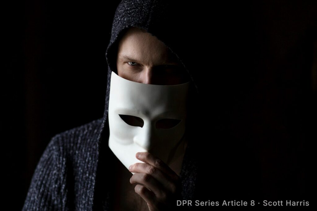 Hooded person holding a blank white mask over their face